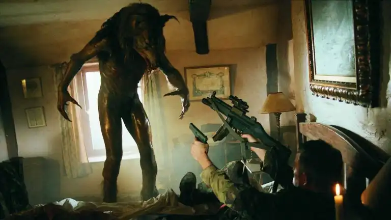 a hulking werewolf, gray and naked with hair only on its head, which is a real-looking wolf head, towers over a man on a bed holding a pistol and an automatic rifle. 