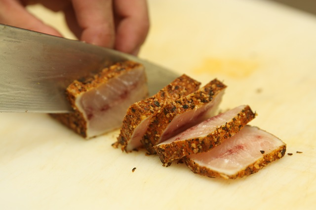 a person slicing cooked sesame-encrusted tuna with a chef's knife