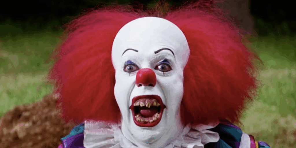 Tim Curry as It, the titular scary clown, smiling with jagged brown teeth and wild eyes