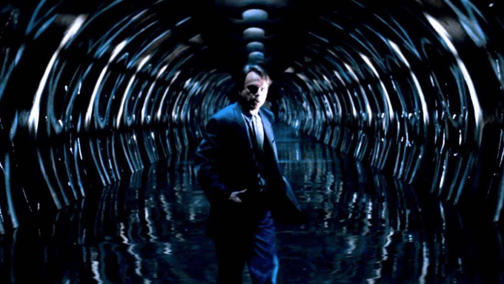 Sam Neil in In The Mouth Of Madness standing in a scary black hallway