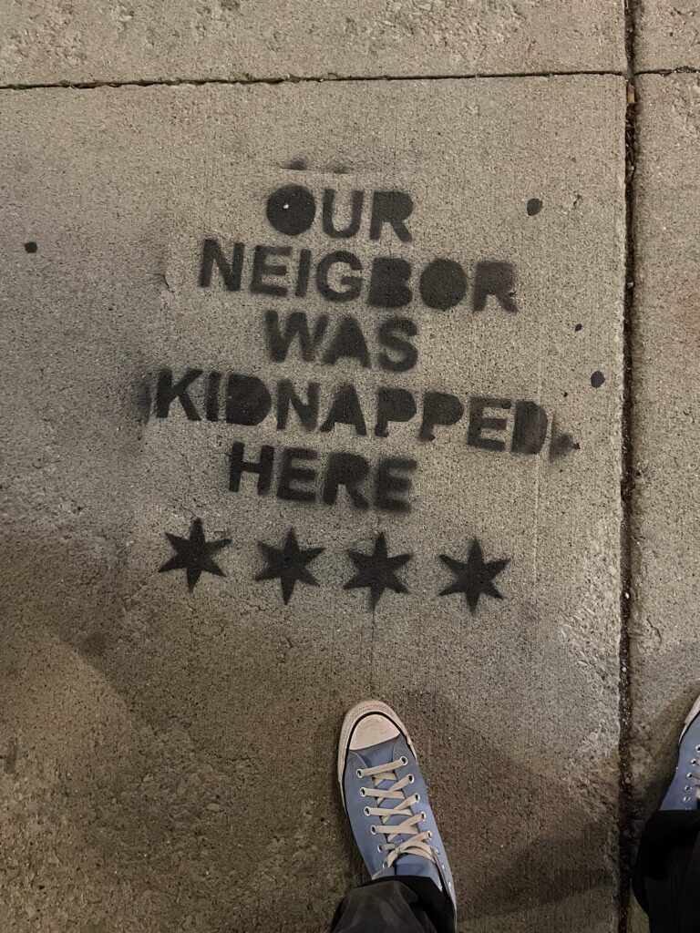 stenciling on a sidewalk reading our neighbor was kidnapped here with four Chicago-style stars underneath