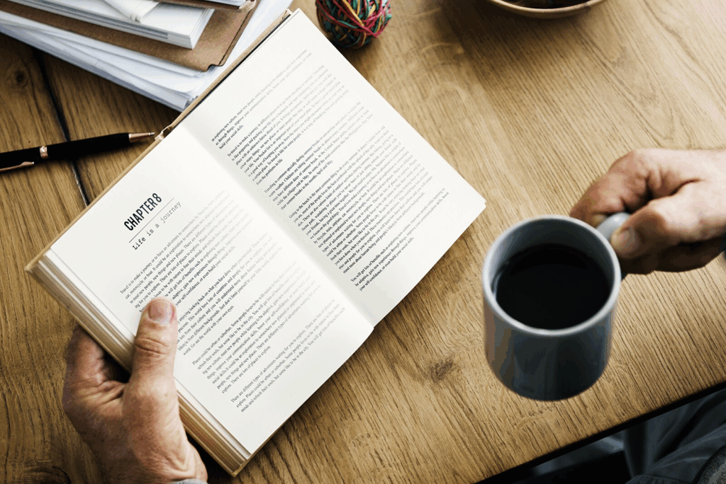 A man reads a book at a cafe in Bangkok while drinking coffee out of a mug
