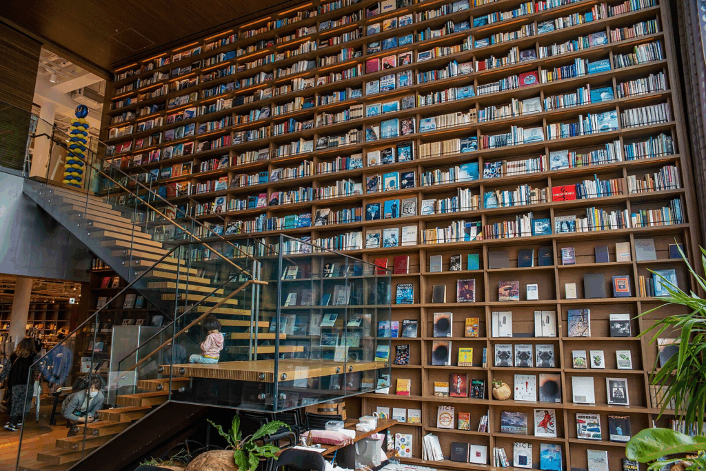 a two story bookstore with high shelves of books and wooden stairs leading to the second floor