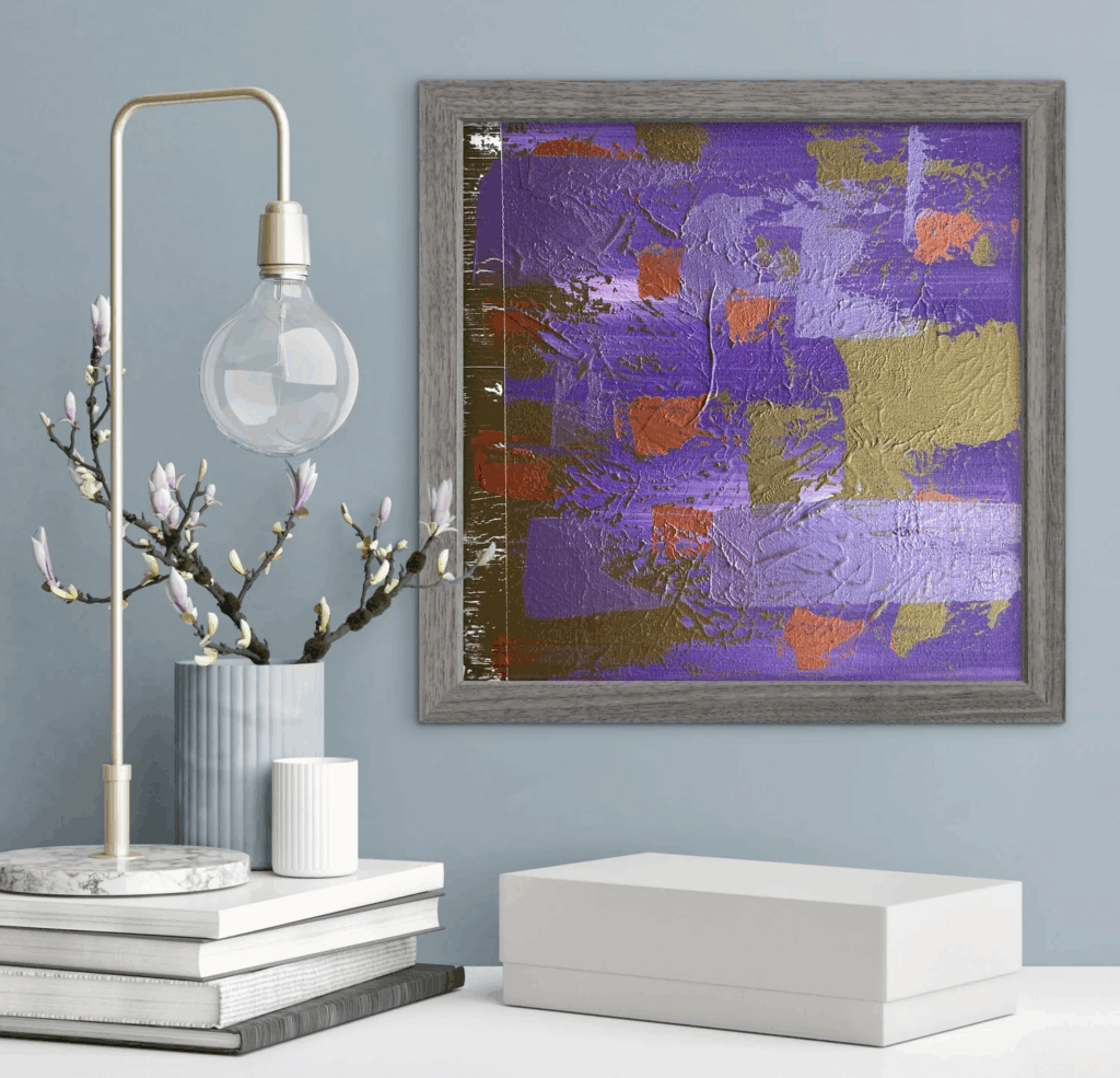 an abstract painting, primarily purple, with slashes of burnt red and squares of brown and mud-gold, sitting in a frame behind a plant and a lamp