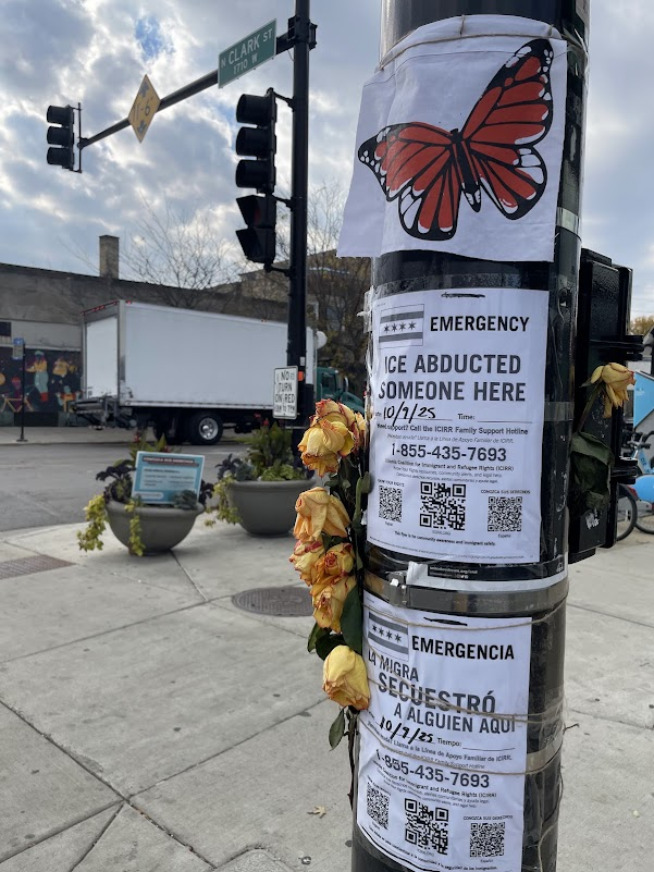 a telephone pole with yellow flowers and a flyer reading EMERGENCY ICE ABDUCTED SOMEONE HERE 10/9/25 Need support? Call the ICIRR Family Support Hotline 1-855-435-7693