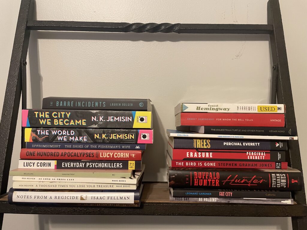 all of the books discussed in this column, stacked on a shelf against a gray wall