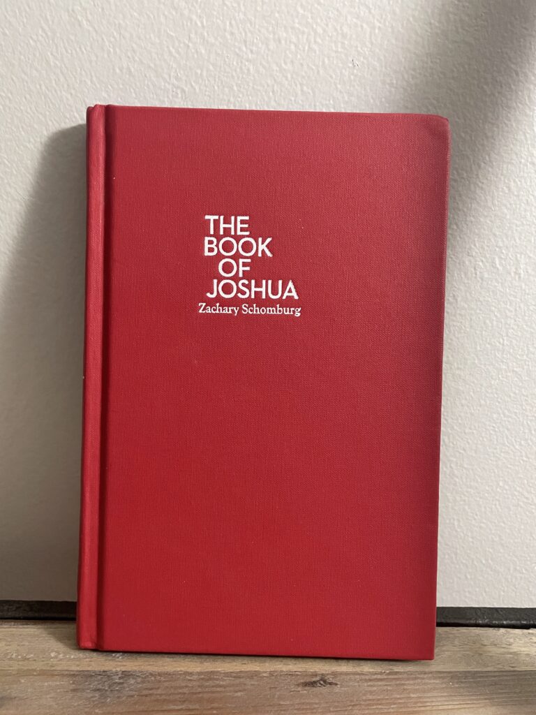 a book, The Book of Joshua by Zachary Schomburg, on a shelf
