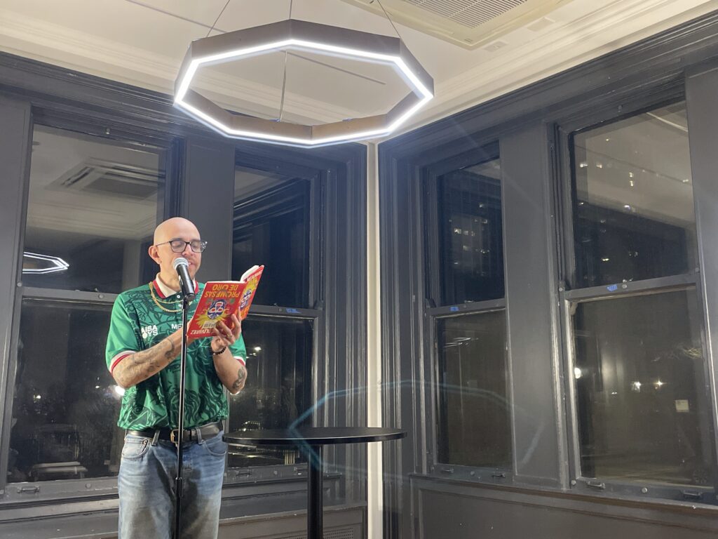 a man in a green Mexico national soccer team jersey and gold chains reads at a microphone
