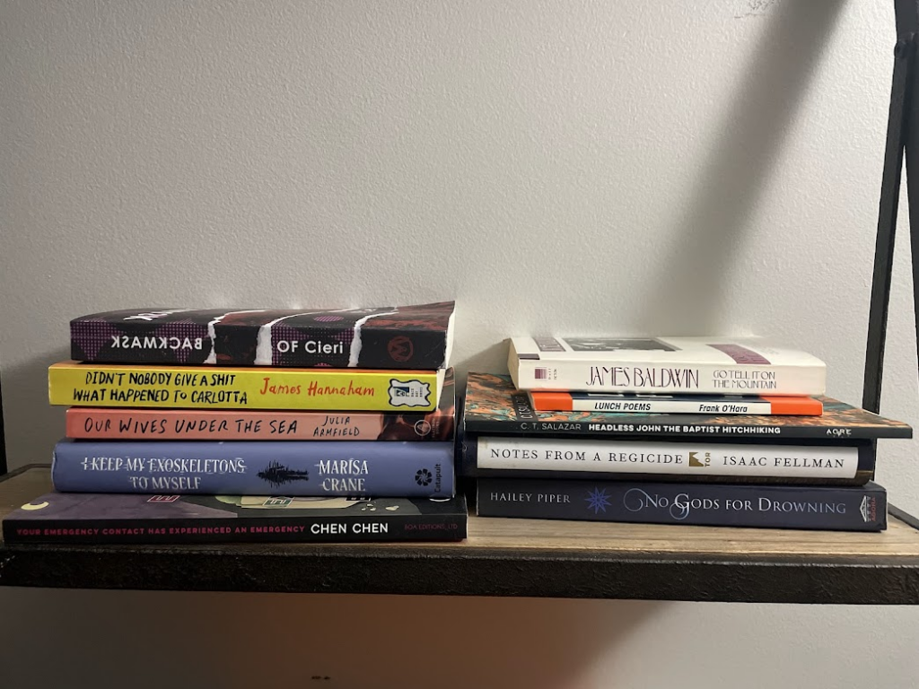 a pile of books on a shelf, including Backmask by OF Cieri, Didn't Nobody Give A Shit What Happened To Carlotta by James Hannaham, Our Wives Under The Sea by Julia Armfield, I Keep My Exeskeletons To Myself by Mac Crane, Your Emergency Contact Has Experienced An Emergency by Chen Chen, Go Tell It On The Mountain by James Baldwin, Lunch Poems by Frank O'Hara, Headless John The Baptist Hitchhiking by C.T. Salazar, Notes From A Regicide by Isaac Fellman, No Gods For Drowning by Hailey Piper