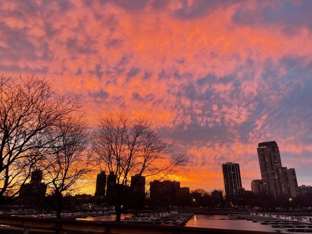 an orange-and-purple sunset fiery above an empty harbor with a city skyline in the background