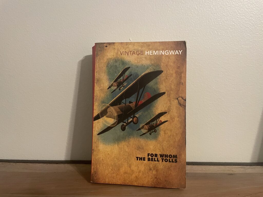 a book, For Whom The Bell Tolls by Ernest Hemingway, on a shelf